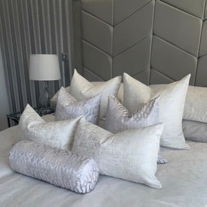 Pu&ograve; includere: Un letto bianco con una testata grigia e una variet&agrave; di cuscini bianchi con un motivo sottile. C'&egrave; un cuscino di supporto bianco e un cuscino cilindrico bianco con lo stesso motivo sottile.