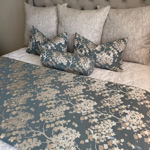 Peut inclure: Un ensemble de lit comprenant un chemin de lit bleu et des coussins assortis avec un motif de branches florales blanches et beiges. L'ensemble inclut un long traversin cylindrique, deux coussins carrés et un chemin rectangulaire sur un couvre-lit blanc.