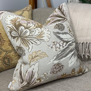 May include: Two decorative throw pillows with a floral pattern in shades of brown, beige, and pink. The pillows are on a light brown sofa.
