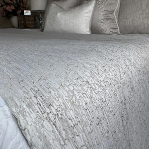 May include: A bed with a silver-grey textured bedspread and matching pillows. The bedspread has a distinctive vertical pattern. The pillows are in varying shades of grey and white. The bedding creates a luxurious look.