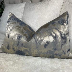 Op de afbeelding: Een decoratief kussen met een abstract patroon in blauw en goud. Het kussen is gemaakt van een zachte, textuurrijke stof en heeft een subtiele glans.