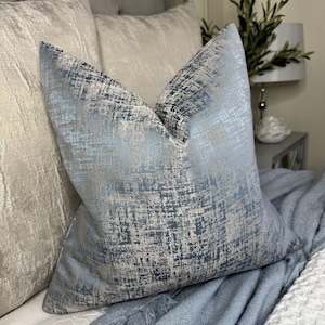 May include: A blue and silver throw pillow with a textured, abstract pattern. The pillow is made of a soft, luxurious fabric and is perfect for adding a touch of elegance to any room.