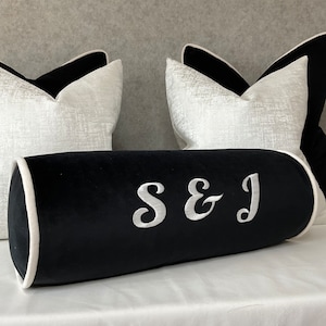 May include: Black velvet bolster cushion with white piping and the initials "S&J" embroidered in white.