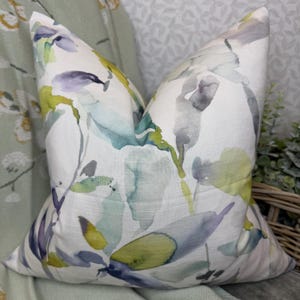 May include: A white throw pillow with a watercolor floral pattern in shades of green, blue, purple, and yellow.