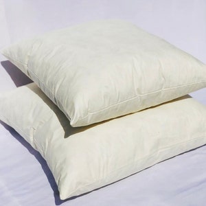 May include: Two white cotton pillow covers stacked on top of each other. The pillow covers are made of a soft, natural fabric and have a simple, elegant design.