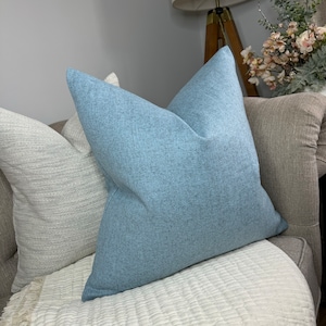 May include: A light blue throw pillow with a textured surface. The pillow is on a white couch with a light gray throw blanket.