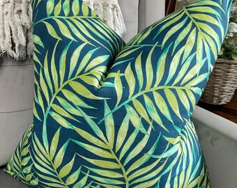 May include: A teal blue cushion with a green tropical leaf pattern. The cushion is made of a soft, textured fabric.