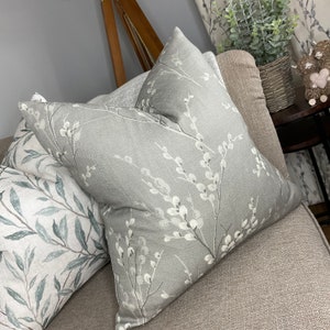 May include: Two decorative throw pillows with a floral pattern. The pillow on the left has a light green and white floral pattern. The pillow on the right has a grey background with a white floral pattern.