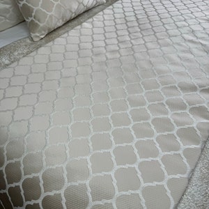 May include: A white bedspread with a subtle embossed geometric pattern. The pattern is a repeating design of squares and circles.