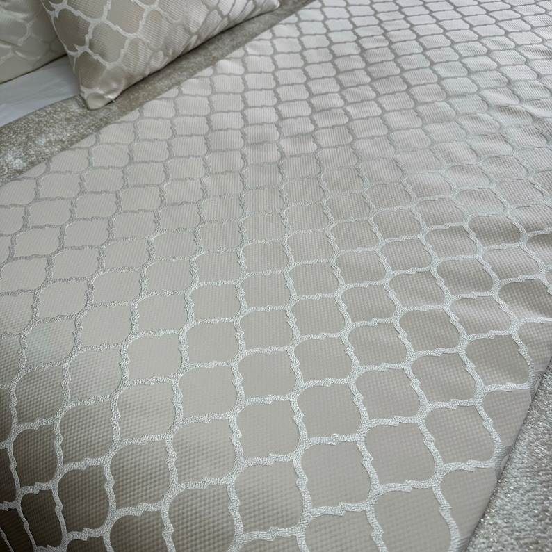 May include: A white bedspread with a subtle embossed geometric pattern. The pattern is a repeating design of squares and circles.