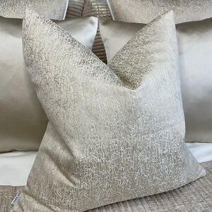 May include: A close-up of a cream-colored pillow with a textured surface. The pillow is made of a soft, luxurious fabric and has a subtle sheen.