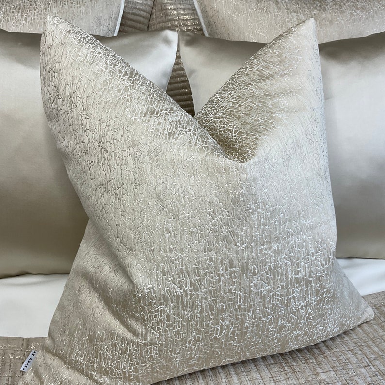 May include: A close-up of a cream-colored pillow with a textured surface. The pillow is made of a soft, luxurious fabric and has a subtle sheen.