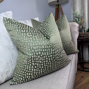 May include: Two green throw pillows with a white speckled pattern on a light grey sofa.