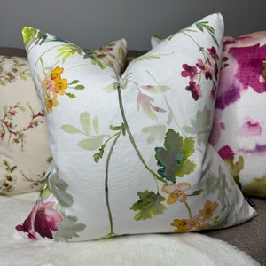May include: A white throw pillow with a watercolor floral pattern featuring pink, yellow, and green flowers and leaves.