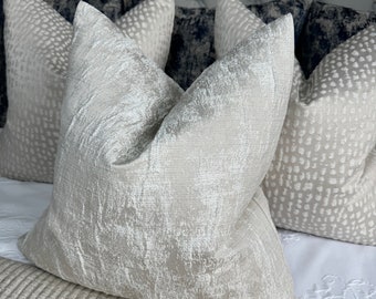 Könnte beinhalten: Ein Set aus drei dekorativen Kissen mit einem strukturierten, metallischen Silber- und Weißstoff. Die Kissen sind auf einem Bett mit einem gesteppten Kopfteil angeordnet.