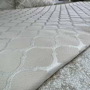 May include: A white bedspread with a subtle embossed pattern of interlocking circles and squares. The pattern is in a light grey colour.