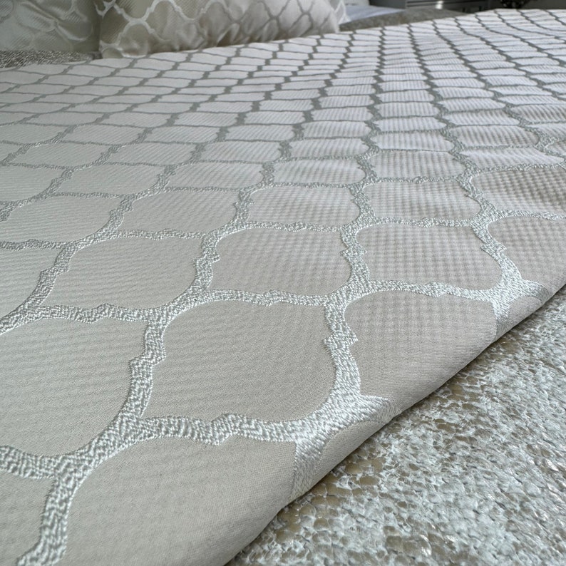 May include: A white bedspread with a subtle embossed pattern of interlocking circles and squares. The pattern is in a light grey colour.