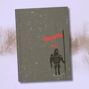 May include: A hardback book with a gray cover featuring a black illustration of a knight holding a flag with a red banner. The background has a snowy effect, and the book is set against a winter scene.