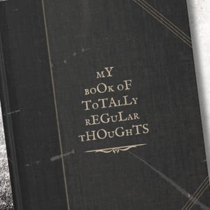 May include: A black book with the text "MY BOOK OF TOTALLY REGULAR THOUGHTS" in white lettering. The book has a distressed, vintage look.