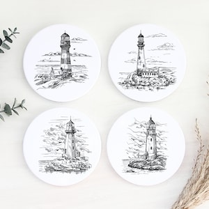 May include: Set of four white ceramic coasters with black and white line drawings of lighthouses on a rocky shore. Each coaster features a different lighthouse design.