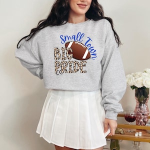May include: A gray sweatshirt with a football graphic and the text "Small Town Big Pride" in blue and black lettering. The football is surrounded by a leopard print design.