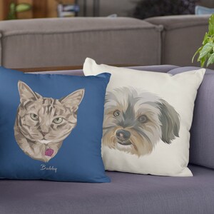 May include: Two custom pet pillows, one with a brown tabby cat with green eyes and a pink collar, and the other with a brown and gray dog with black eyes. The cat pillow is blue with the name "Bubby" printed on it. The dog pillow is white.