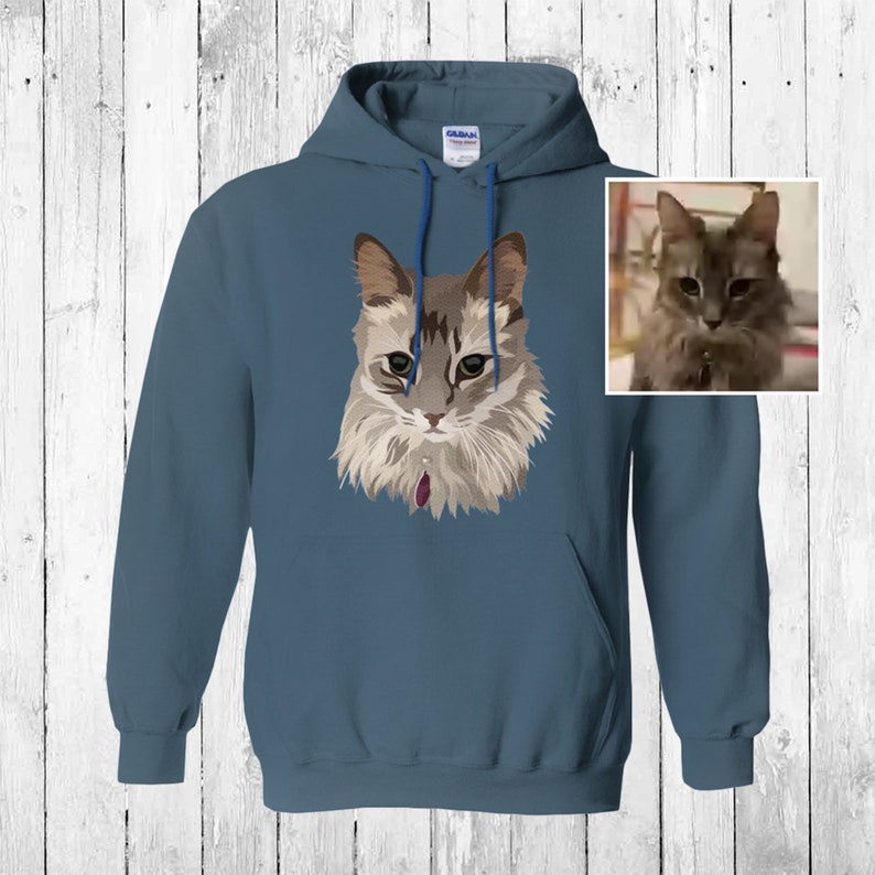 May include: A blue hooded sweatshirt with a stylized illustration of a cat on the front. The cat has gray and white fur and green eyes.