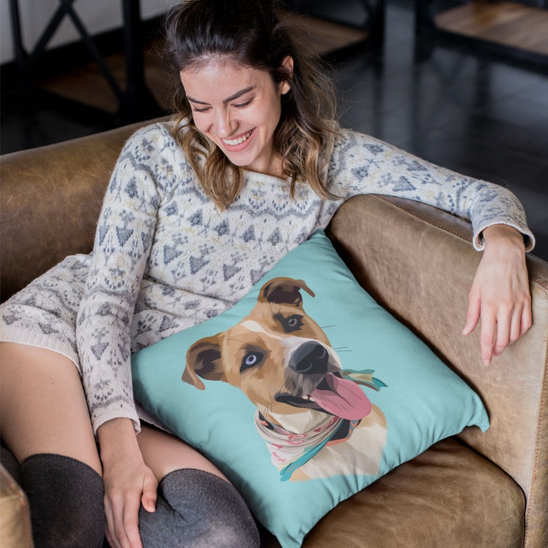 May include: A turquoise blue throw pillow with a cartoon illustration of a dog with brown and white fur, blue eyes, and a pink bandana. The dog is sticking its tongue out and has a happy expression.