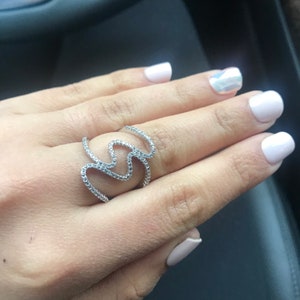 May include: A silver ring with a wavy design set with small clear stones.