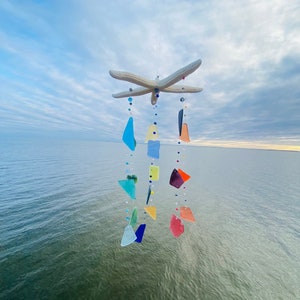 May include: A colorful glass and bead wind chime featuring a starfish design hangs from a string against a blue sky and water background.