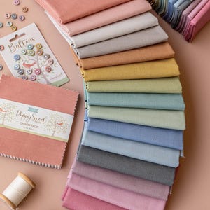 Peut inclure: Un assortiment de carrés de tissu colorés, de boutons et de bobines de fil. Les carrés de tissu sont dans diverses nuances de rose, de bleu, de gris et de jaune. Les boutons sont petits et colorés. Les bobines de fil sont blanches, bleues et pêche.
