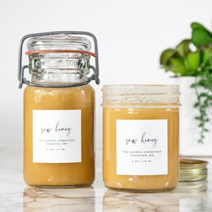 May include: Two glass jars of raw honey with white labels that read "raw honey" and "The Hanson Homestead, Shakopee, MN 4 oz | 118 ml".