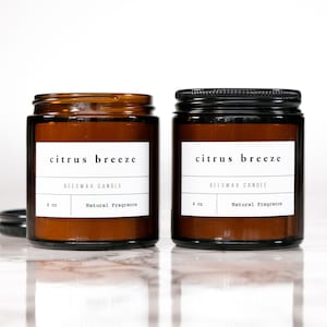 May include: Two amber glass jars with black lids containing beeswax candles. The labels on the jars read "citrus breeze beeswax candle 4 oz natural fragrance".
