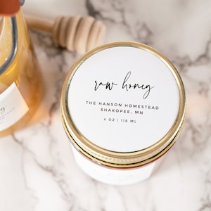 May include: A glass jar of raw honey with a white label that reads "raw honey", "THE HANSON HOMESTEAD", "SHAKOPEE, MN", and "4 OZ | 118 ML".
