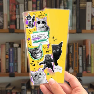 May include: A rectangular yellow bookmark featuring a collage of black and white cat photographs, small star and heart icons, and a quote that reads: I have studied many philosophers and many cats. The wisdom of cats is infinitely superior.