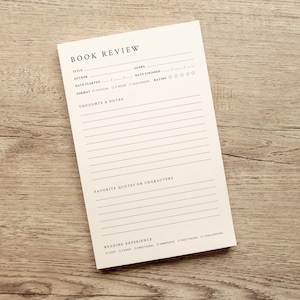 May include: A rectangular cream-colored book review notepad featuring black printed text and lines. The layout includes sections for title, author, genre, dates, format, rating, thoughts and notes, favorite quotes or characters, and reading experience.