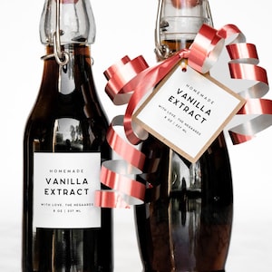 May include: Two glass bottles of homemade vanilla extract with swing-top closures. Each bottle has a white label with black text. One bottle is adorned with a red and white ribbon and a tag that reads "Vanilla Extract".