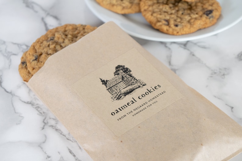 May include: A brown paper bag with a label that says "oatmeal cookies from the negard homestead homemade for you". The label has a black and white illustration of a cabin with trees.