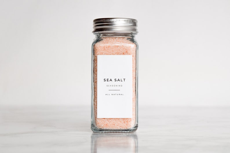 May include: A glass jar with a silver lid filled with pink sea salt. The jar has a white label that reads "SEA SALT SEASONING ALL NATURAL".