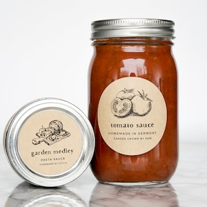 May include: Two glass jars with brown paper labels. The larger jar contains tomato sauce and has a label that reads "tomato sauce, homemade in Vermont, garden grown by Sam". The smaller jar contains pasta sauce and has a label that reads "garden medley, pasta sauce, homemade by Lottie".