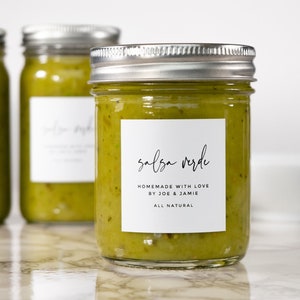 Op de afbeelding: Drie glazen potten gevuld met groene salsa verde. De voorste pot heeft een wit etiket met zwarte tekst waarop staat "salsa verde, zelfgemaakt met liefde door Joe & Jamie, volledig natuurlijk".