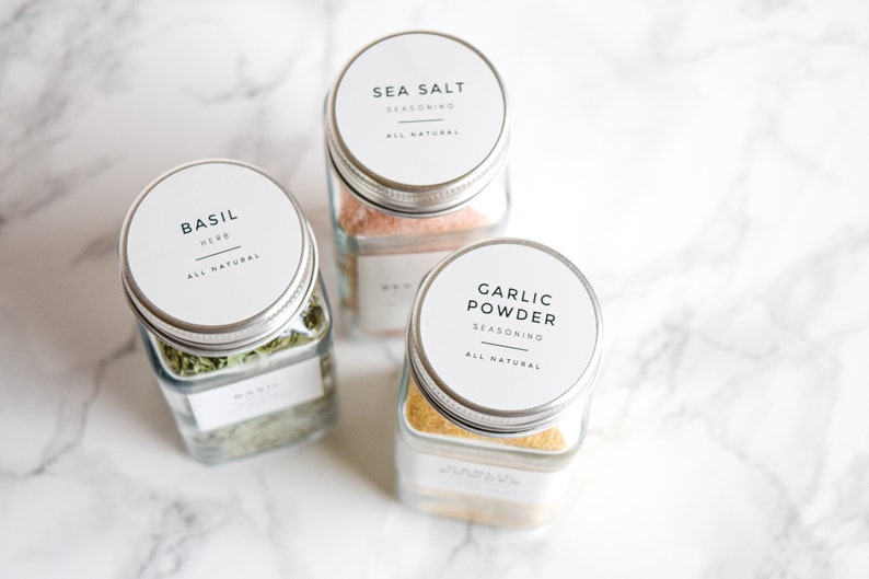 May include: Three glass spice jars with silver lids and white labels. The labels have black text that reads "Basil Herb All Natural", "Sea Salt Seasoning All Natural", and "Garlic Powder Seasoning All Natural".