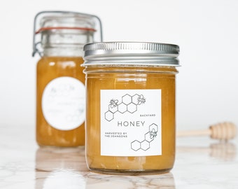 May include: Two glass jars of honey with white labels. The label on the front jar reads "Backyard Honey, Harvested by The Johnsons". The label features a black and white illustration of a honeycomb with bees.