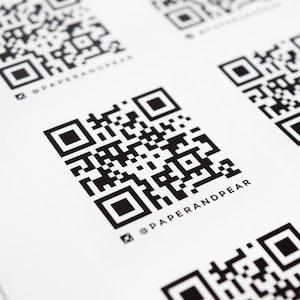 Peut inclure: Gros plan sur plusieurs autocollants carrés blancs avec des codes QR noirs et le texte "@PAPERANDPEAR" imprimé sous chaque code.
