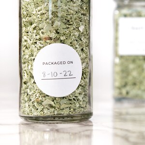 May include: A clear glass jar filled with dried herbs with a white round label that says "PACKAGED ON 8-10-22".