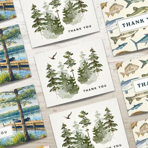 May include: Assortment of "Thank You" cards with various nature-themed designs. Some cards feature a lake scene with a dock and trees, while others display watercolor pine trees or fish patterns. Each card has the words "Thank You".