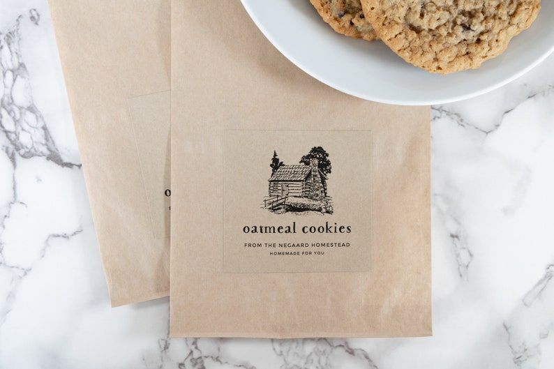 May include: A brown paper bag with a sticker that says "oatmeal cookies from the Negaard Homestead homemade for you". The sticker features a black and white illustration of a cabin in the woods.