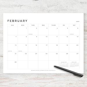 May include: A minimalist white calendar page for February 2027, with a simple black font. The days of the week are across the top, with dates in a grid. A black pen rests on the bottom right corner. The calendar is designed and printed in Minnesota.