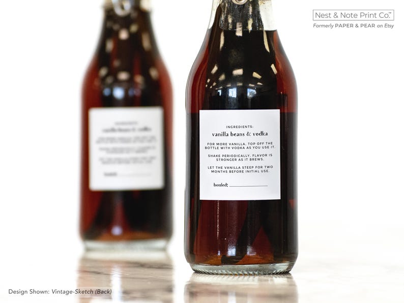 May include: Two glass bottles filled with a dark liquid, likely a vanilla extract or similar product. Each bottle has a white label with black text detailing ingredients and instructions. The text on the label reads "vanilla beans & vodka".