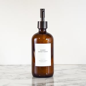 May include: A brown glass bottle with a black pump dispenser filled with hand sanitiser. The bottle has a white label with the text "HAND SANITIZER" and "WATERLESS CLEANSER 10 oz (295 ml)".